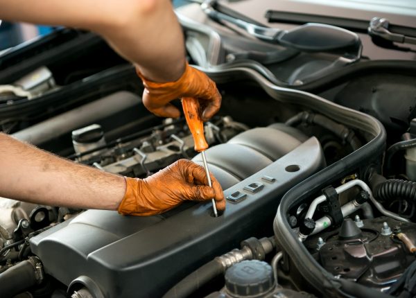 Close up of the gloved hands of a male mechanic working on a car engine with a screw driver in a workshop during a service