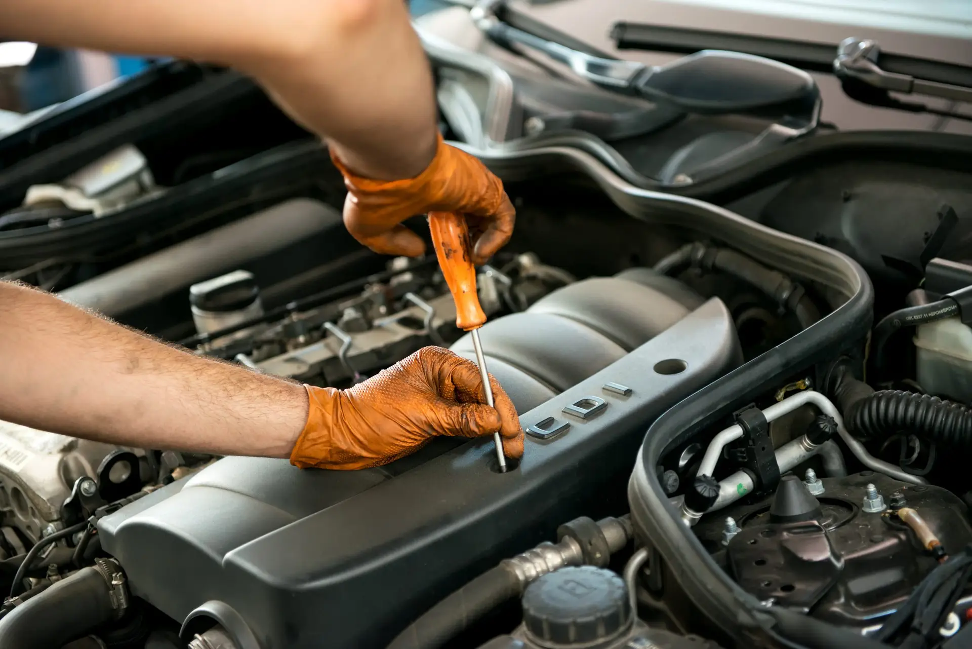 Close up of the gloved hands of a male mechanic working on a car engine with a screw driver in a workshop during a service