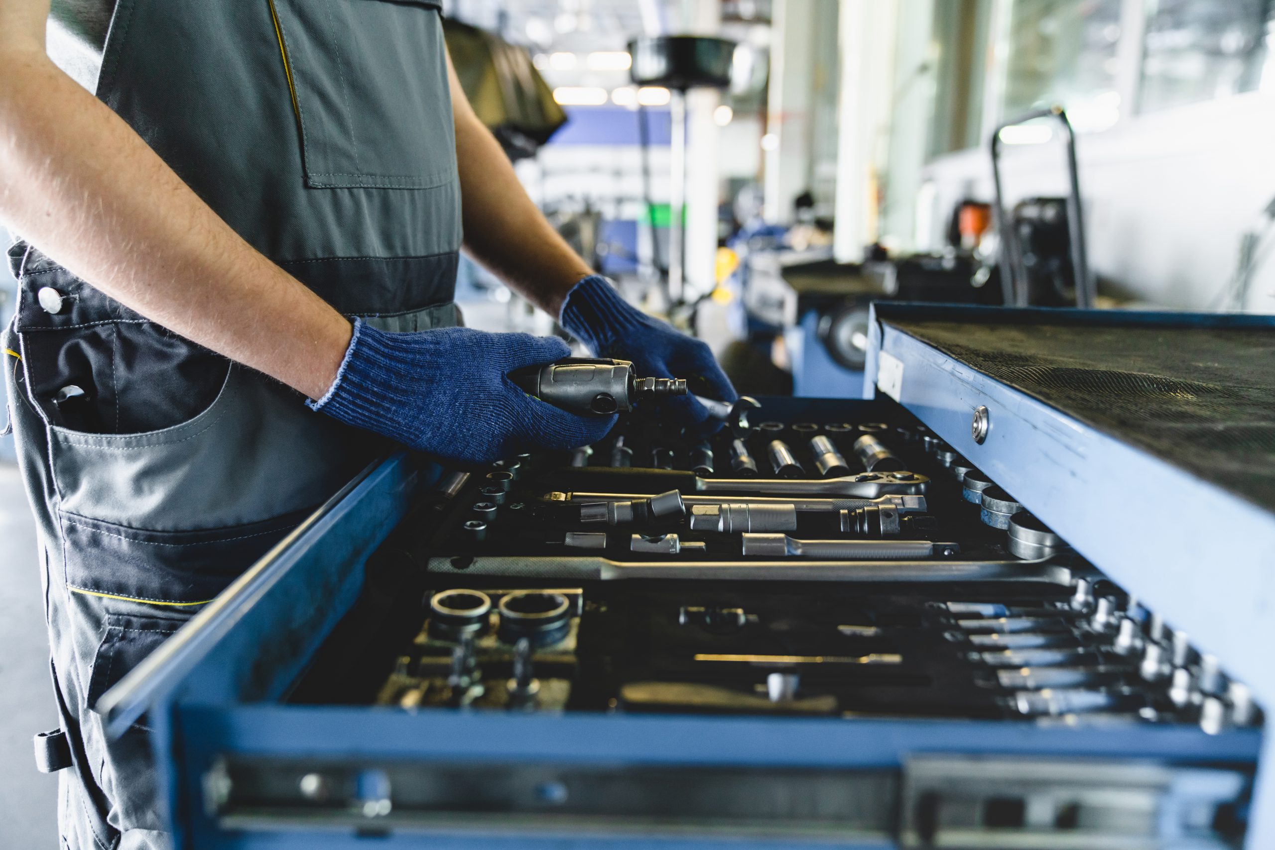 Closeup vehicle inspection service MOT concept. Caucasian male technician mechanic in special robe uniform fixing repairing car while looking for tools instruments