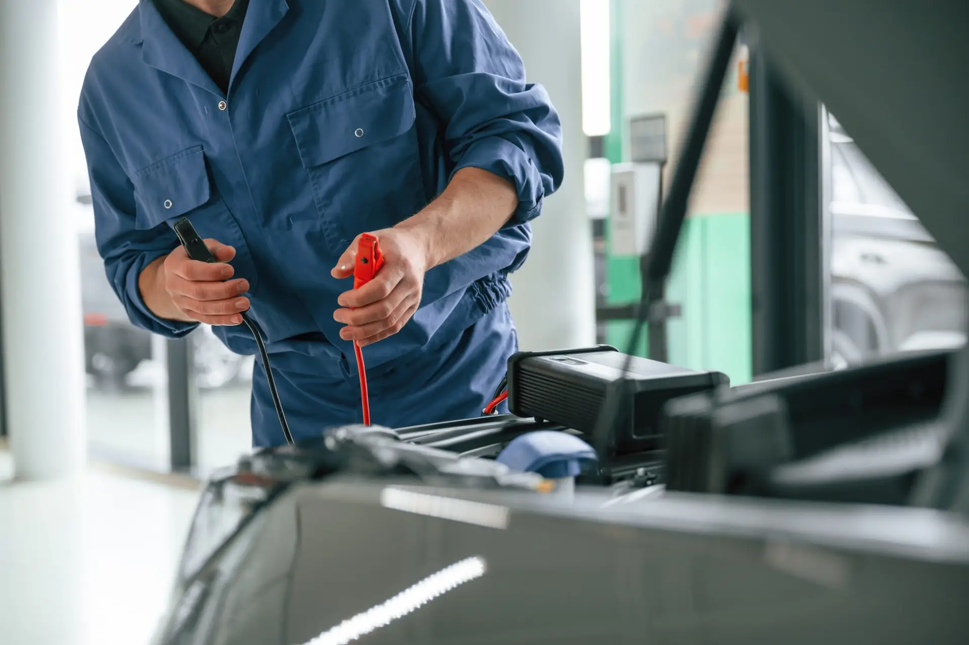 With hood opened. Man in blue uniform is working in the car service.